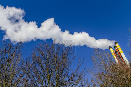 Photo for Dynamic angle of chimney from a refuse incinerator emitting smoke and polluting the air against a clear blue sky. - Royalty Free Image