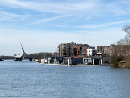 Pintoresca vista se despliega sobre el río, capturando el puente Prins Clausbrug y el desarrollo de viviendas de Stadswerven en Dordrecht, personificando la mezcla de tradición y modernidad de la ciudad.