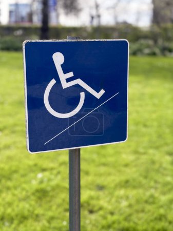 Un pequeño letrero azul para discapacitados en silla de ruedas se coloca sobre un fondo borroso del jardín, simbolizando la accesibilidad y la inclusividad en espacios al aire libre.