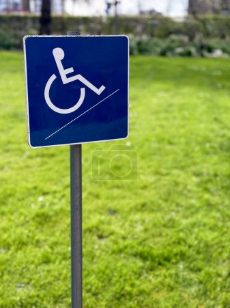 Un petit panneau bleu pour handicapés en fauteuil roulant se dresse sur un fond de jardin flou, symbolisant l'accessibilité et l'inclusion dans les espaces extérieurs.