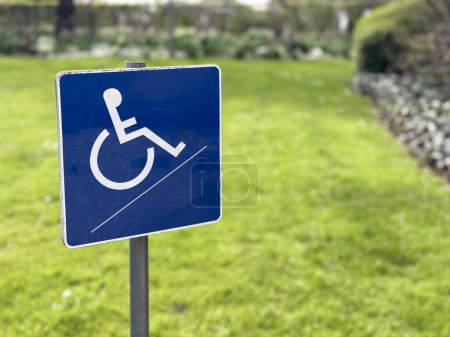 Ein kleines blaues Behindertenschild für Rollstuhlfahrer steht vor verschwommenem Gartenhintergrund und symbolisiert Barrierefreiheit und Inklusion im Außenbereich.