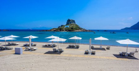 Téléchargez les photos : Chaise longue et parasol sur la belle plage d'Agios Stefanos en face du paradis Île de Kastri- ruines historiques et paysages paradisiaques à la côte de l'île de Kos, Grèce - en image libre de droit