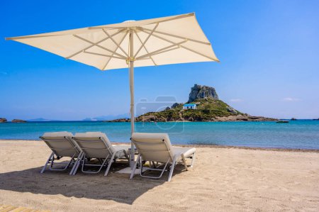 Foto de Silla de cubierta y sombrilla en la hermosa playa de Agios Stefanos frente al paraíso Island Kastri- ruinas históricas y paisajes paradisíacos en la costa de la isla de Kos, Grecia - Imagen libre de derechos