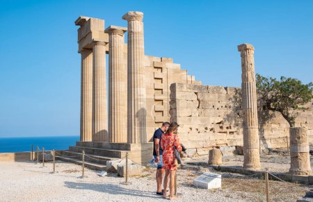 Téléchargez les photos : Lindos, Grèce - 24 mai 2023 : Un couple debout devant la ruine du temple d'Athéna lisant une plaque - en image libre de droit