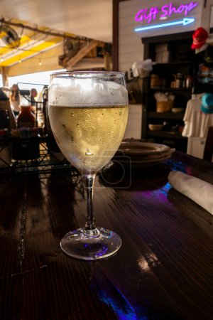 A Glass of Chilled White Wine on the Table of a Lively Restaurant and Its Gift Shop