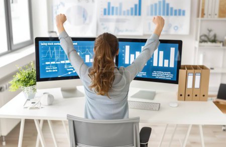 In this inspiring image, a woman exudes confidence and determination as she celebrates a profitable trade on the stock market from the comfort of her desk. With arms raised in triumph, she embodies the spirit of empowerment and financial independence
