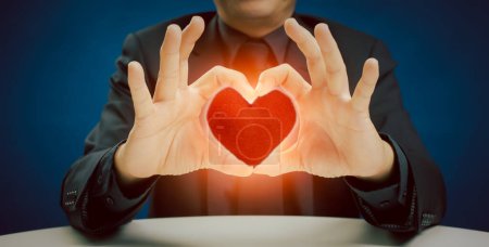 Photo for Businessman in suit showing hands sign gesture with red heart shape pillow on blue background in the studio. take care of health, being in love and service mind business concept - Royalty Free Image