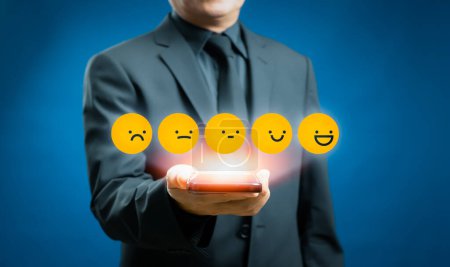 Téléchargez les photos : Un homme d'affaires ou un client donne une note à l'expérience de service sur écran tactile virtuel et réfléchit à l'émoticône du visage pour examiner le sondage de satisfaction, concept d'évaluation du service à la clientèle - en image libre de droit