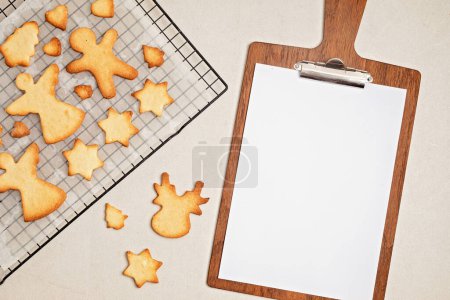 Foto de Proceso de cocción de galletas de Navidad y tablón de clips con hoja de papel. Dulces caseros, Mockup para la receta, idea festiva del postre del bricolaje - Imagen libre de derechos