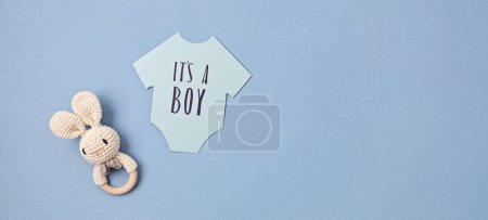 Foto de Baby shower, gender reveal party. It's a boy message over paper cut onesie. Flatlay, top view on a blue pastel background. Newborn gifts. Invitation, celebration, greeting card idea - Imagen libre de derechos