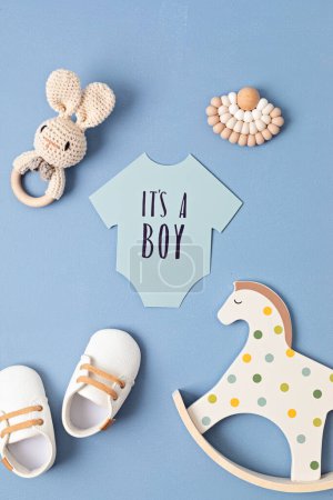 Foto de Baby shower, gender reveal party. It's a boy message over paper cut onesie. Flatlay, top view. Newborn gifts. Invitation, - Imagen libre de derechos