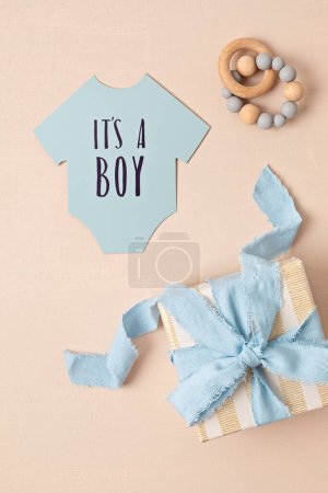 Foto de Baby shower, gender reveal party. It's a boy message over paper cut onesie. Flatlay, top view. Newborn gifts. Invitation, - Imagen libre de derechos
