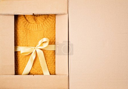 Téléchargez les photos : Boîte de livraison déballante avec pull orange chaud à l'intérieur. Shopping en ligne, cadeaux pour les vacances saisonnières d'automne et d'hiver, Noël - en image libre de droit