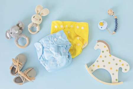 Téléchargez les photos : Pose plate avec couche bébé en tissu réutilisable, jouets et accessoires. Couche écologique sur fond bleu pastel. Style de vie durable, idée zéro déchet - en image libre de droit