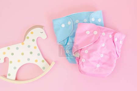 Photo for Flat lay with reusable cloth baby diaper and toy rocking horse. Eco friendly nappy on pink pastel background. Sustainable lifestyle, zero waste idea - Royalty Free Image