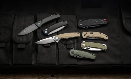 Modern universal pocket folding knives. Penknives lie on a canvas cover with pockets. Dark background.