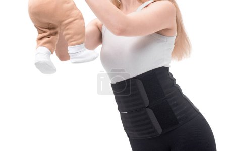 Después de dar a luz, una mujer usa un cinturón médico para sostener su abdomen y pelvis mientras sostiene a su bebé. Aislado sobre fondo blanco.