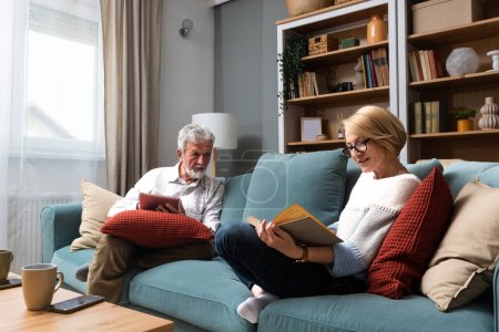 Una vida sencilla. Feliz de mediana edad pareja de personas mayores de 70 años marido y mujer sentarse relajarse en el sofá en la sala de estar lectura libro beber té juntos, la calma de edad avanzada 60 pareja de amantes del libro descansar en casa disfrutar de la vida