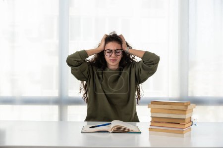 Photo for Overworked. Tired young lady sit at home desk crowded with books hide face in palms feeling headache migraine. Exhausted female student feeling bad losing concentration unable to learn study - Royalty Free Image