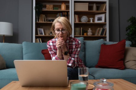 Müde gestresste ältere Frau mittleren Alters, die sich nach der Computerarbeit krank fühlt, sitzt zu Hause auf dem Sofa, traurig müde alte Seniorin Großmutter, die an Kopfschmerzen leidet Migräne