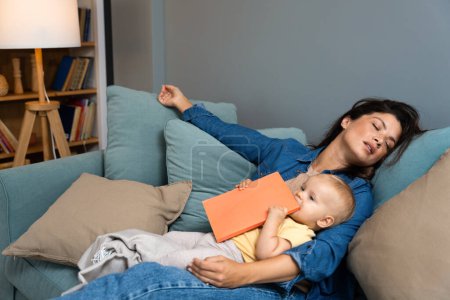 Young mother fell asleep after reading fairy tale story book to her baby. Tired mommy sleeping with her child in her lap tried to read to her kid in the evening time. Single mom concept.