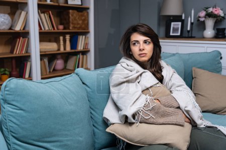 Photo for Caucasian sad woman sitting at the sofa with depression. Young student female suffering from mental burnout, feeling depressed, wrapped in blanket, sits alone in silence at her home. - Royalty Free Image