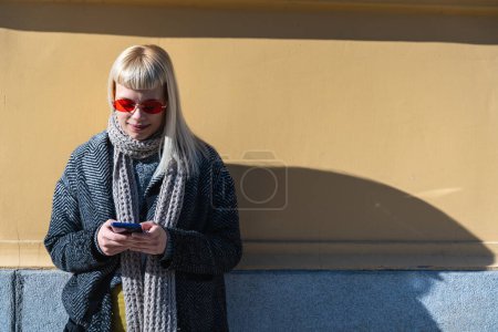 Junge fröhliche Hippie-Hipster in coolen Klamotten mit lustigen Brillen, die sich im Freien an eine Hauswand in der Stadtstraße lehnen, halten Handy-Chats in sozialen Netzwerken ab. Menschen urbanes Lifestyle-Konzept.
