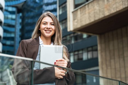 Young business woman freelance motivational speaker life coach standing in front of office building with digital tablet preparing for staff meeting. Businessperson product strategy expert waiting
