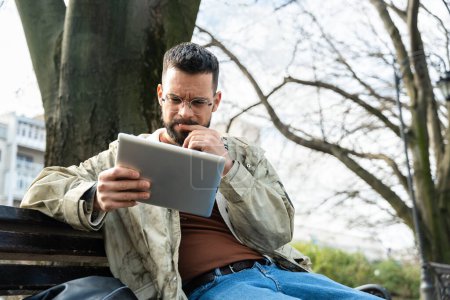 Junge Hipster Millennial Man Weltreisende nomadischen Lebensstil sitzen im Freien mit digitalen Tablet, um nach neuen Reisezielen und Orten zu suchen zu besuchen. Männliches Konzept der Generation Z im Ausland