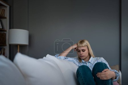Mujer triste caucásica sentada en el sofá con depresión. Joven estudiante mujer que sufre de agotamiento mental, sensación de depresión, dificultades de relación, se sienta sola en silencio en su casa.