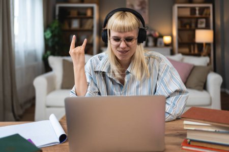Young hipster university student woman listening heavy metal rock and roll or hard core music on wireless headphones using books and laptop for study and learning at home for educational exam