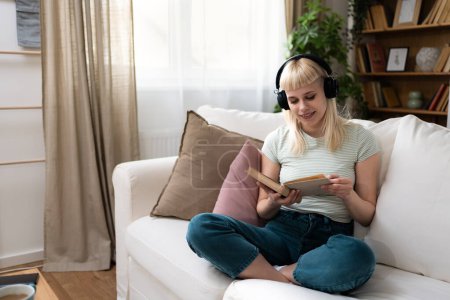 Jeune femme se relaxant sur un canapé à la maison. Écouter de la musique sur un casque sans fil et lire un livre. Amoureux de livres femme profiter du temps libre et des activités de week-end pour la détente dans son appartement confortable