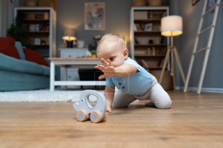 Photo for Young happy adorable baby girl or boy sitting on the floor of apartment playing with his or her favorite toy. Cute child crawling at home floor play alone and having fun. - Royalty Free Image