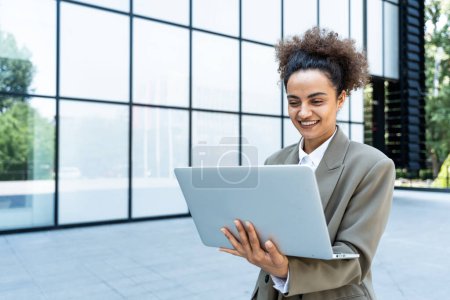 Porträt einer jungen erfolgreichen Bürokauffrau mit Laptop außerhalb des Bürogebäudes in formeller Kleidung. Professionelle Unternehmerin, die online im Freien arbeitet und Informationen überprüft