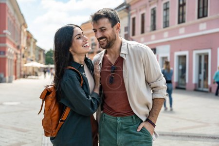 Young happy hipster backpacker travelers couple, visiting new country, summer travel destination, enjoying their vacation, walking down the city streets, looking historical buildings and architecture.