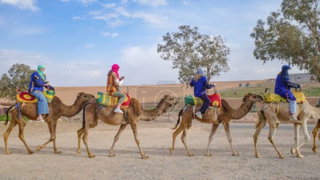 Photo for Marrakech, Morocco - Feb 22, 2023: Tourists ride Dromedary camels through the Agafay desert - Royalty Free Image
