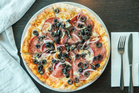 Photo for Delicious italian pizza on the table with black olives, onion and ham - Royalty Free Image