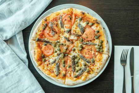 Téléchargez les photos : Pizza italienne avec anchois, sardines et tomates sur une table en bois avec serviette, couverts et nappe - en image libre de droit