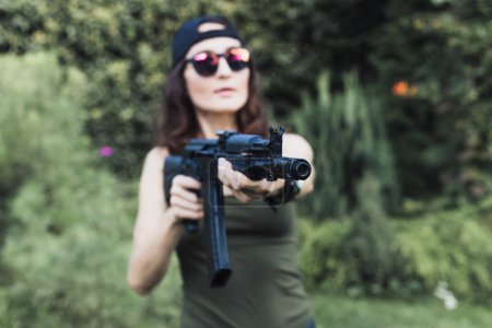 Foto de Hermosas fuerzas especiales de mujeres jóvenes y serias que sostienen el rifle automático Kalashnikov AKM (enfoque en el cañón delante del arma) - Imagen libre de derechos