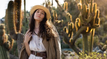 Photo for A portrait of stunning brunette woman in a Western-style desert landscape with cacti. Concept of beauty and travel. Image with big copy space. - Royalty Free Image