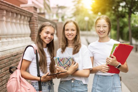 Foto de Retrato de tres adolescentes felices (14-15 años) caminando a la escuela, llevando libros y cuadernos. Concepto de regreso a la escuela, educación y crecimiento. - Imagen libre de derechos