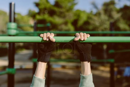 Foto de Primer plano de las manos femeninas con guantes deportivos. Persona que cuelga en la barra horizontal al aire libre. - Imagen libre de derechos