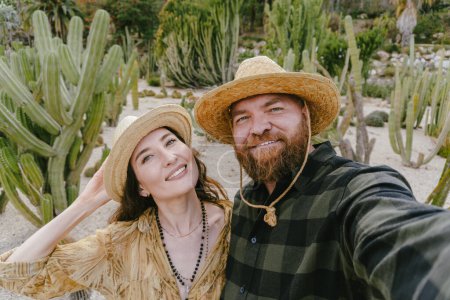 Téléchargez les photos : Portrait d'un couple souriant dans un paysage désertique de style occidental avec des cactus. Selfie ensemble pendant les vacances en Amérique latine. Concept voyage et lune de miel. - en image libre de droit