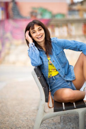 Téléchargez les photos : Portrait de belle jeune femme insouciante se détendre sur le banc en plein air en ville - en image libre de droit