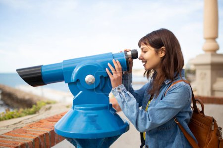 Téléchargez les photos : Portrait latéral de jeune femme regardant à travers le télescope à vue de mer - en image libre de droit