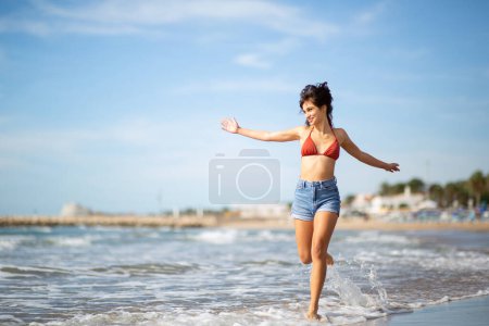 Téléchargez les photos : Portrait pleine longueur de belle jeune femme courant sur le bord de la mer avec les bras tendus - en image libre de droit