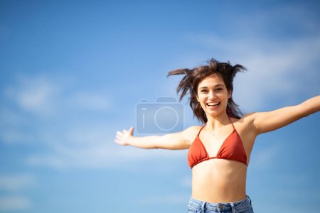 Portrait of attractive young woman in bikini standing with hands outstretched against sky on a summer day