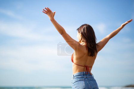 Photo for Rear view portrait of young woman standing with hands outstretched on beach against sky on a summer day - Royalty Free Image