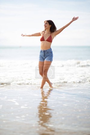 Foto de Retrato de cuerpo completo de una joven excitada caminando por la playa con los brazos extendidos - Imagen libre de derechos