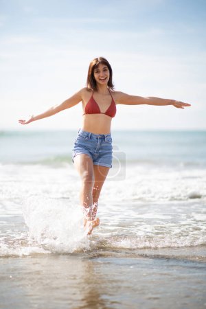 Photo for Full body portrait of cheerful young woman walking on the beach with arms outstretched - Royalty Free Image